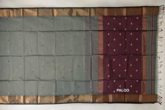 Sage green silk cotton saree laid flat, with small triangular motifs, dark sage green patterned borders and a deep wine maroon pallu with tassels.