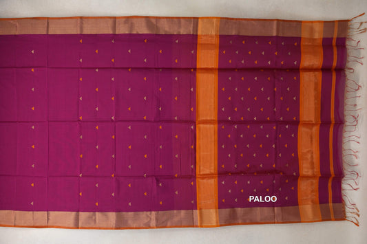 Deep magenta Maheshwari silk cotton saree laid flat, showing a pallu with scattered triangular motifs, orange bands and a fringed edge.
