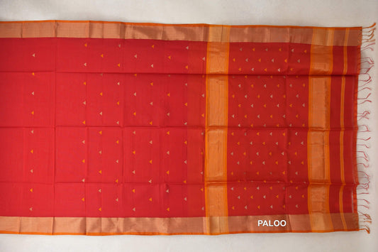 Tomato red Maheshwari silk cotton saree spread flat, with small triangular motifs, deep orange borders and a striped pallu with tassels at the right.