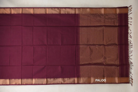 Deep wine Maheshwari silk-cotton saree laid flat, with a plain body, copper-toned borders and a broad pallu with tassels.