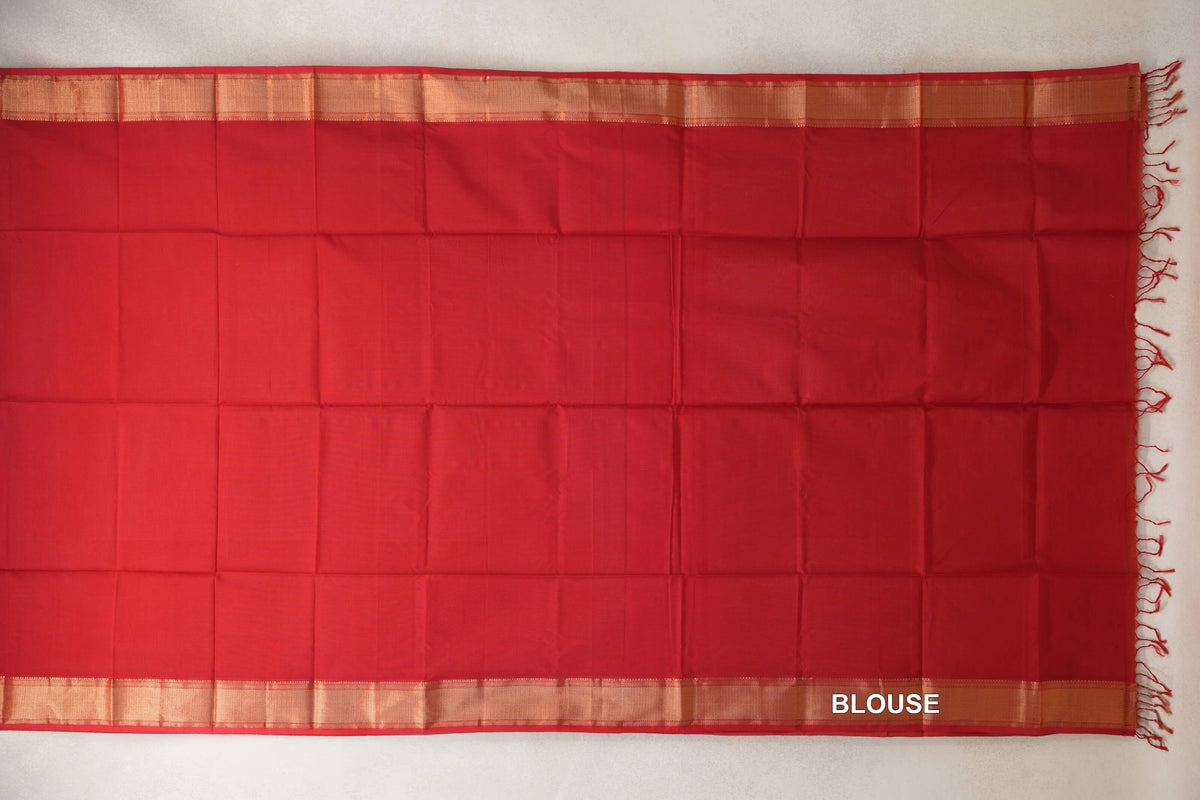 Vermilion red Maheshwari silk cotton blouse piece laid flat, with copper-toned borders along the top and bottom and red tassels at one end.