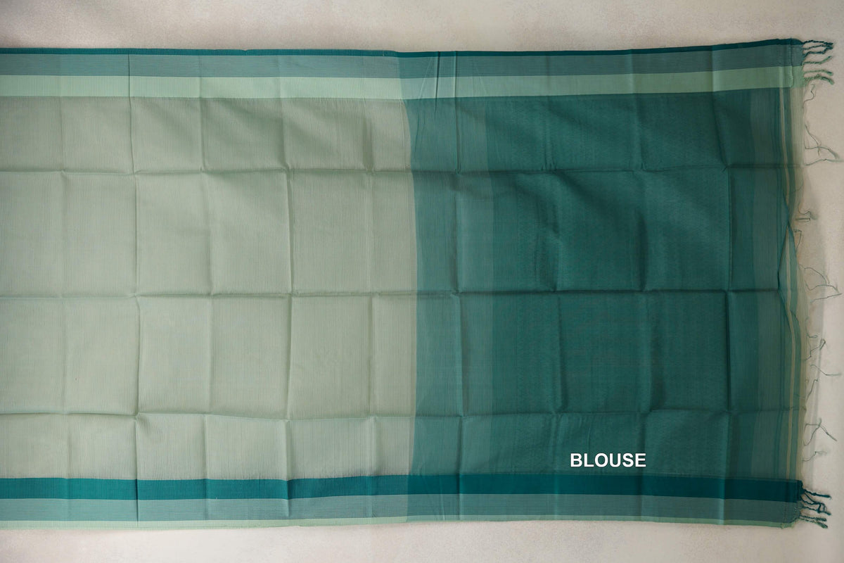 Pale sage green silk cotton saree laid flat with a deep teal green blouse section, light sage borders, teal selvedge stripes and tassels.
