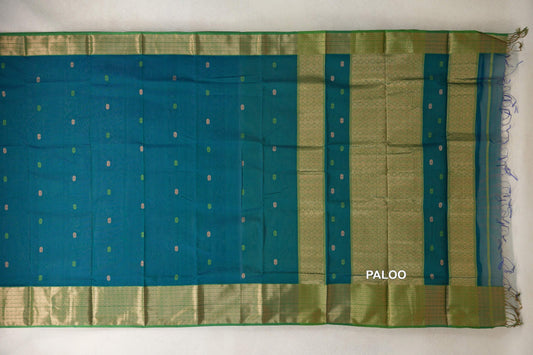 Maheshwari silk cotton saree spread flat, with a teal blue body dotted with small motifs, leaf green patterned borders and a geometric, fringed pallu.