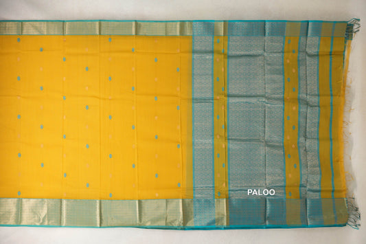 Maheshwari silk cotton saree laid flat, with a mango yellow body, small scattered motifs, and turquoise blue patterned borders and pallu with tassels.