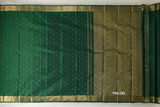 Bottle green Kanjivaram silk saree spread out, with gold dots across the body, broad gold borders and an ornate floral and geometric pallu at right.