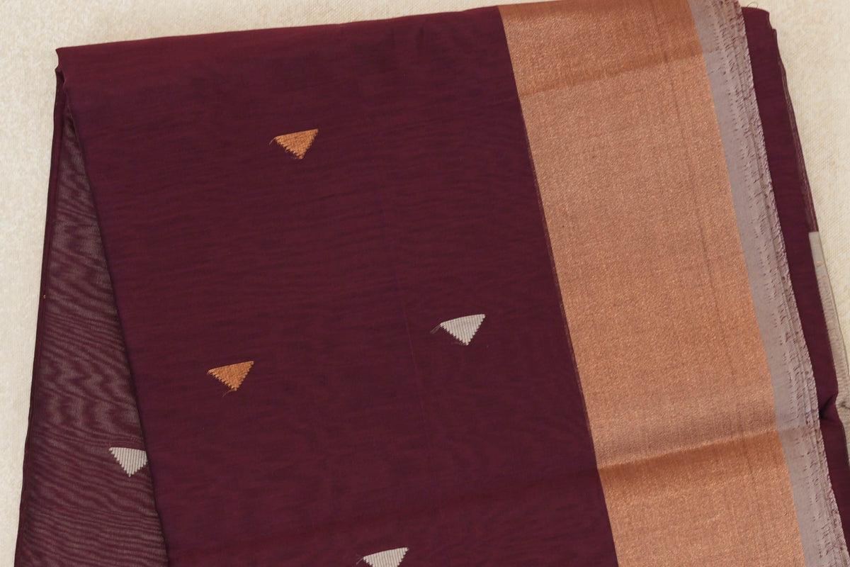 Folded deep wine maroon Maheshwari silk cotton saree with small triangular accents, a broad shimmering border and silver grey selvedge.
