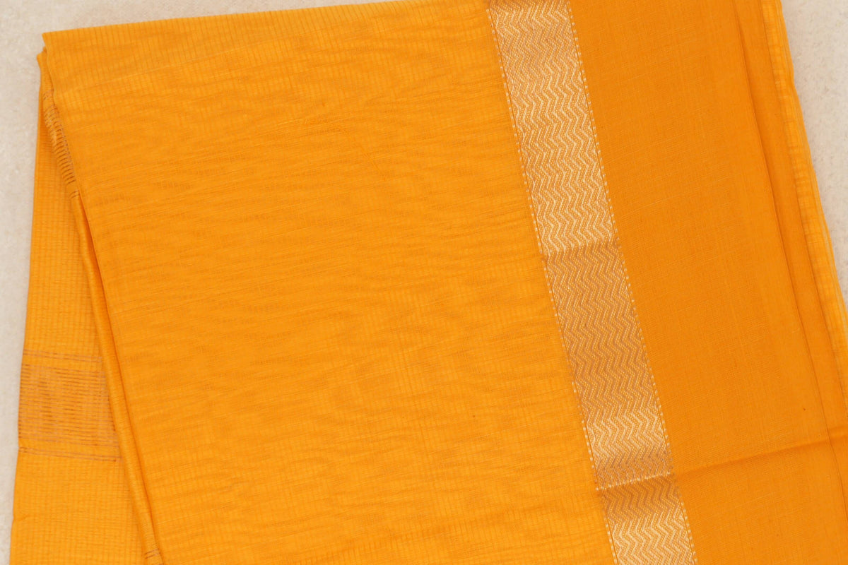 Folded mango yellow Maheshwari silk cotton saree with a subtly textured body and a shimmering zigzag-patterned stripe.