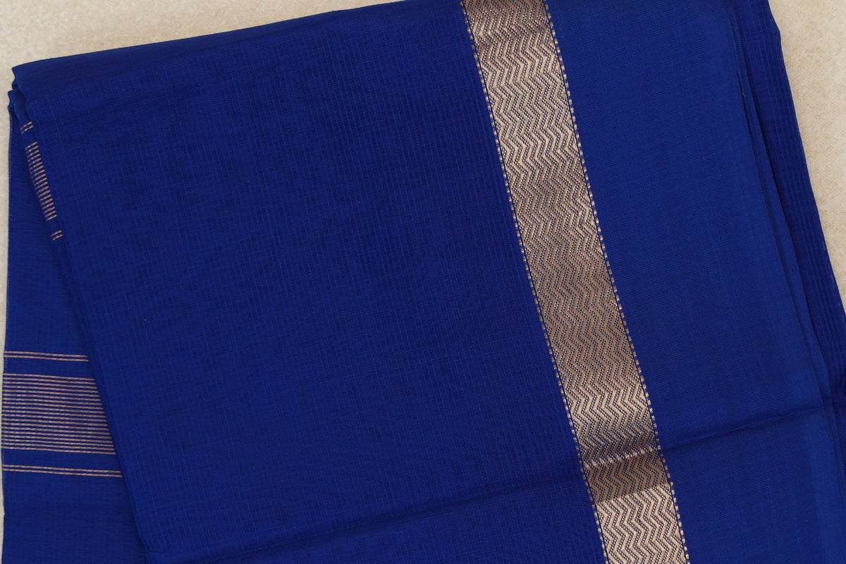Folded deep royal blue Maheshwari silk cotton saree with a subtle checked texture, a metallic wavy band and fine stripes at one edge.
