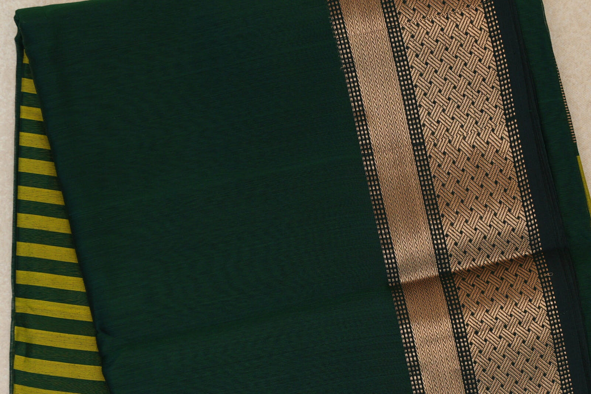Folded bottle green Maheshwari silk cotton saree with a broad patterned deep green border and olive yellow stripes peeking from beneath.
