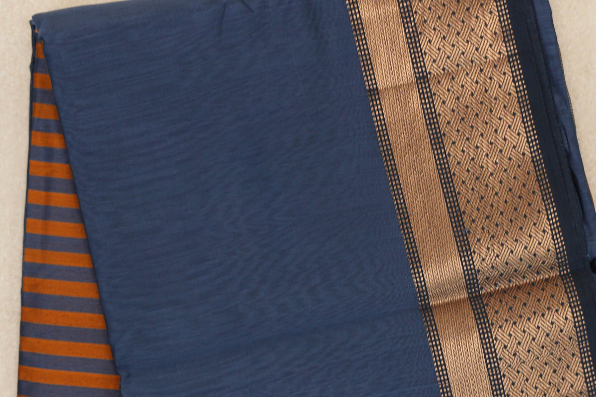 Folded dark grey blue Maheshwari silk cotton saree with deep orange pallu stripes peeking out on the left and a gold-toned patterned border on the right.