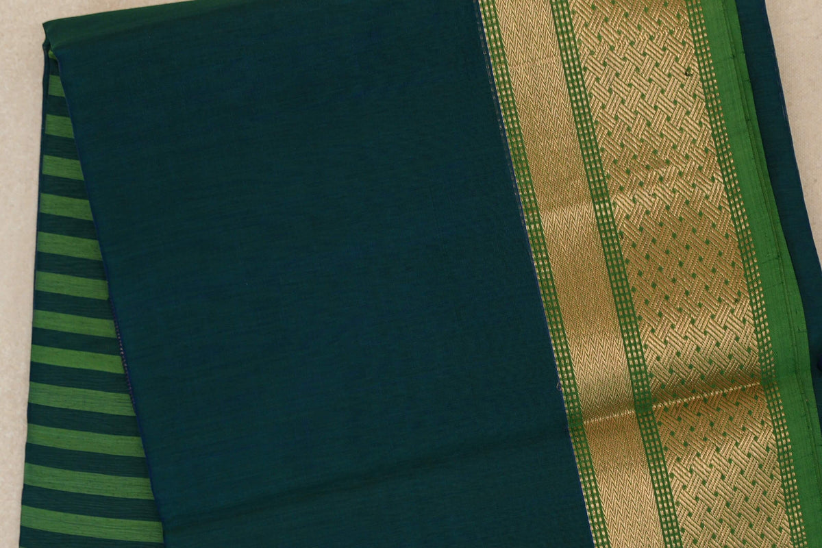 Folded Maheshwari silk cotton saree with a peacock blue body, leaf green striped pallu at left and a gold-toned patterned border at right.