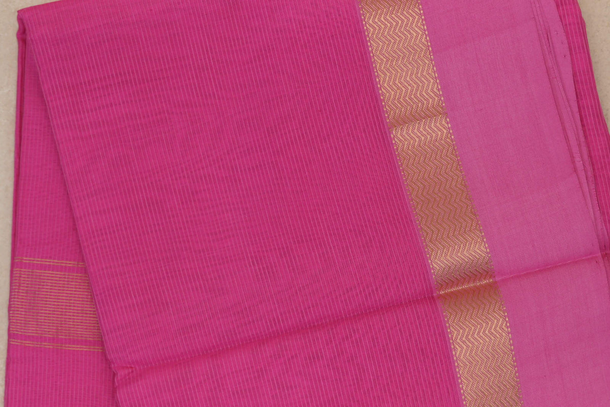 Folded bright rani pink Maheshwari silk cotton saree with fine vertical stripes, a gold wavy border and narrow gold stripes at one edge.