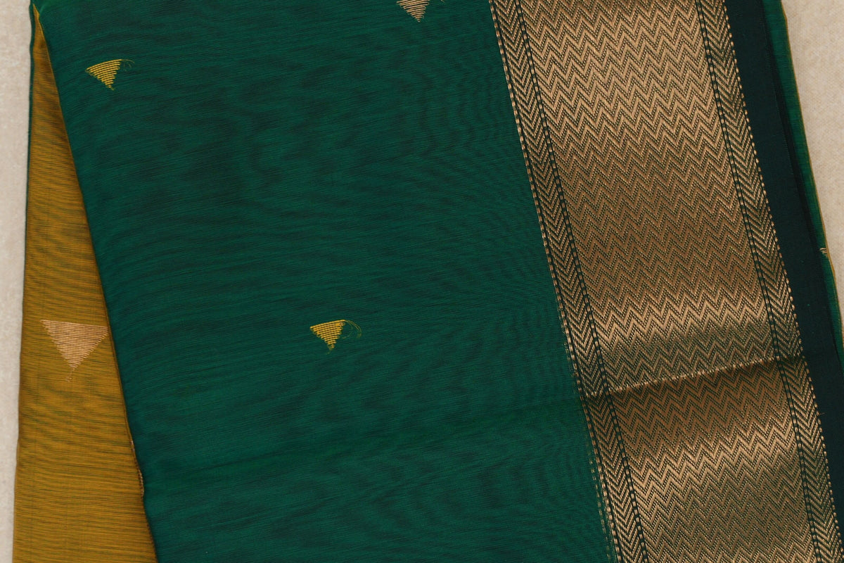 Close-up of a folded bottle green Maheshwari silk cotton saree with small gold triangular motifs, a chevron-patterned border and mustard yellow fabric beneath.