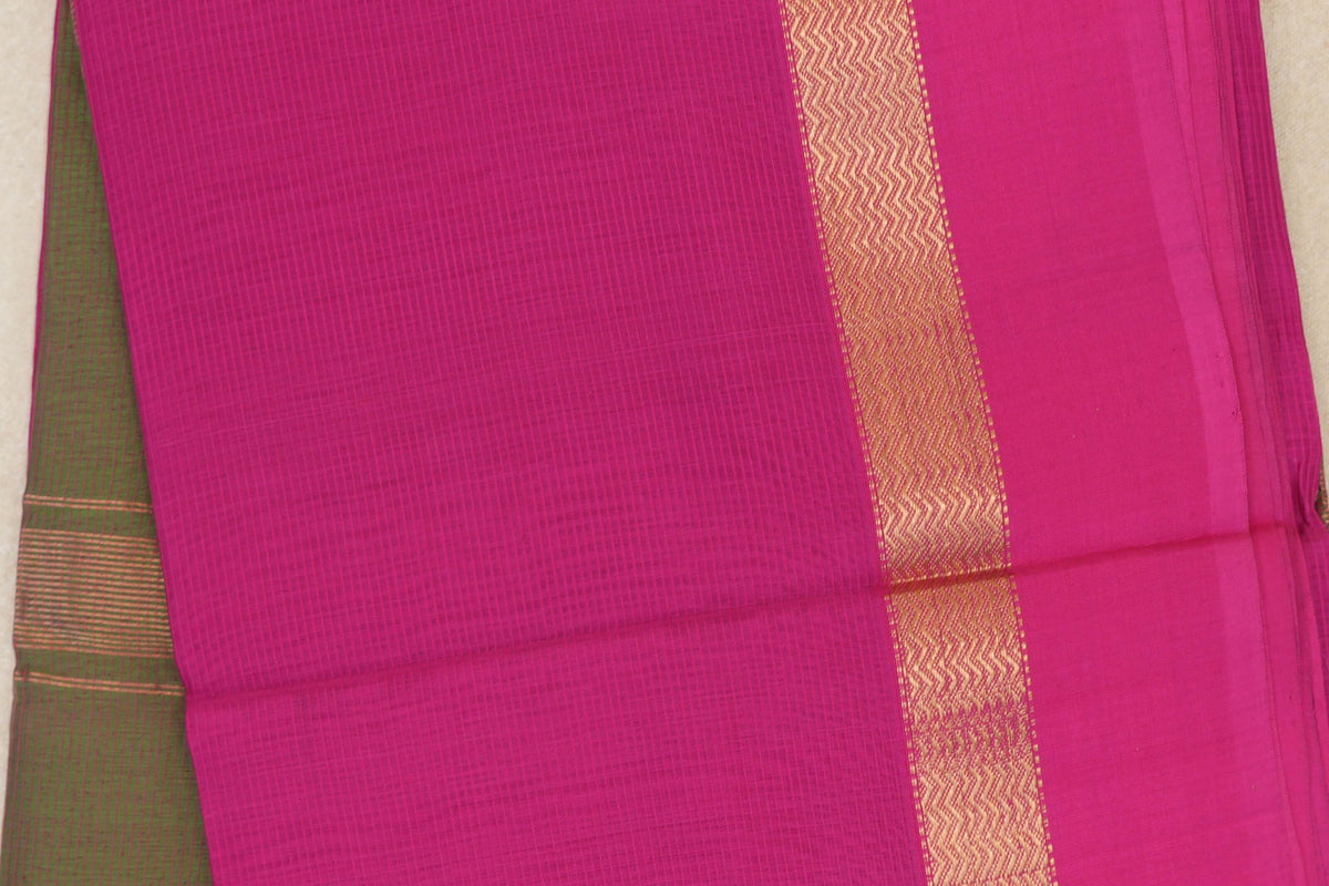 Close-up of a rani pink Maheshwari silk cotton saree with a fine checked body, a gold zigzag border and olive green fabric peeking out at the left.
