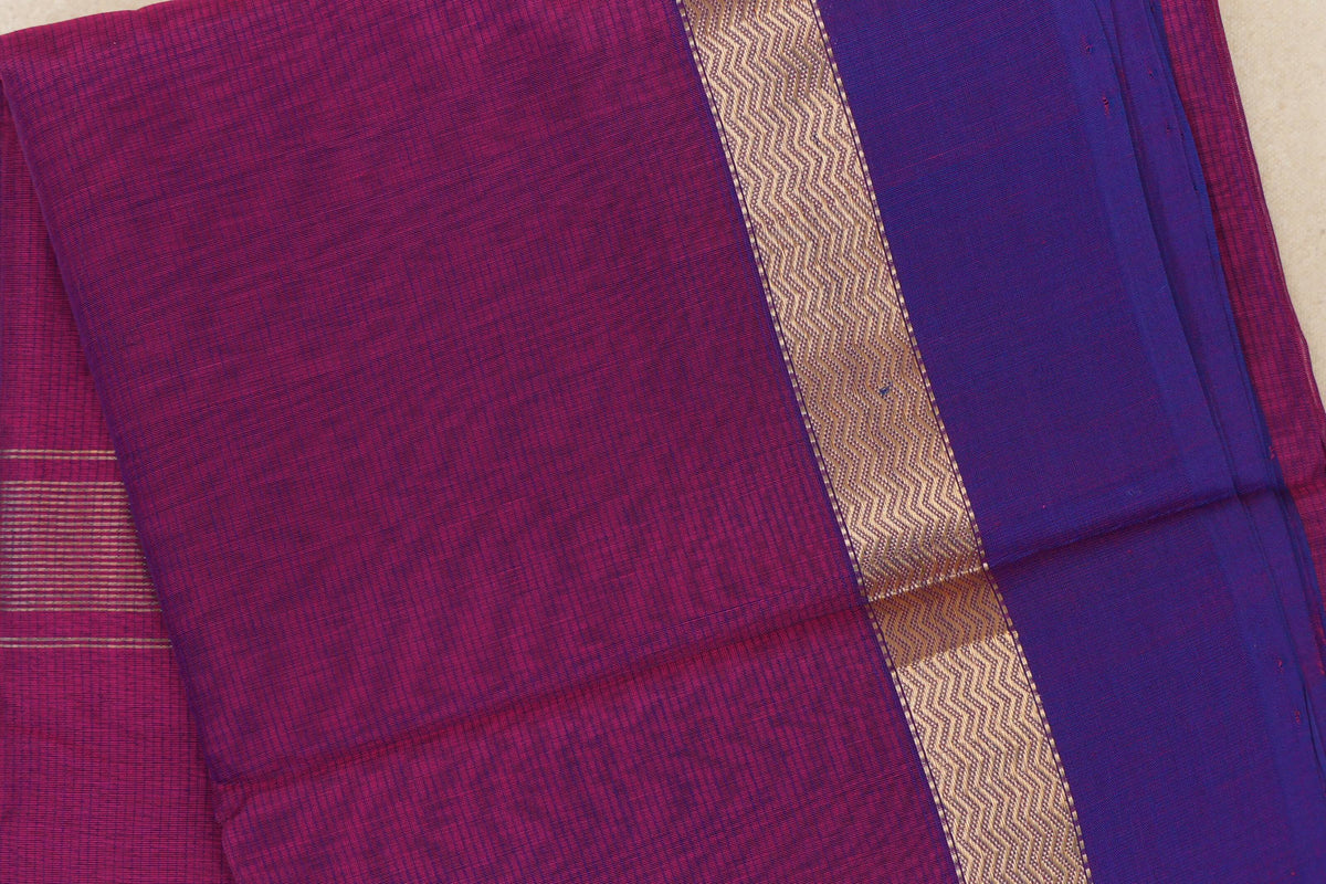 Folded Maheshwari silk cotton saree showing a deep magenta body, violet purple border and a gold-toned wavy patterned band.