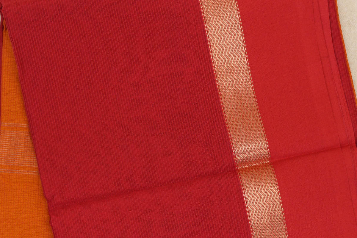 Close-up of a red Maheshwari silk cotton saree with fine vertical stripes, a gold-coloured zigzag border and orange fabric visible beneath.