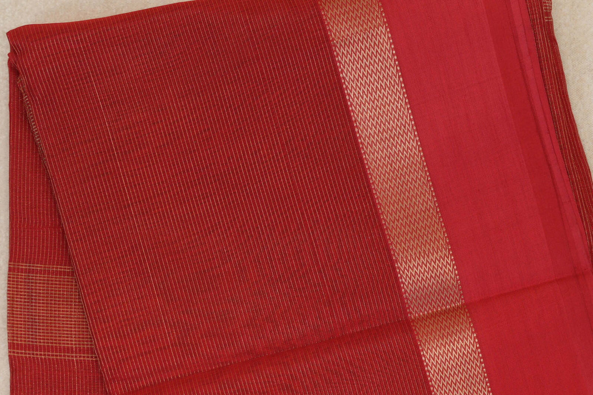Folded tomato red Maheshwari silk cotton saree with fine gold stripes, a geometric gold border and a plain red section.