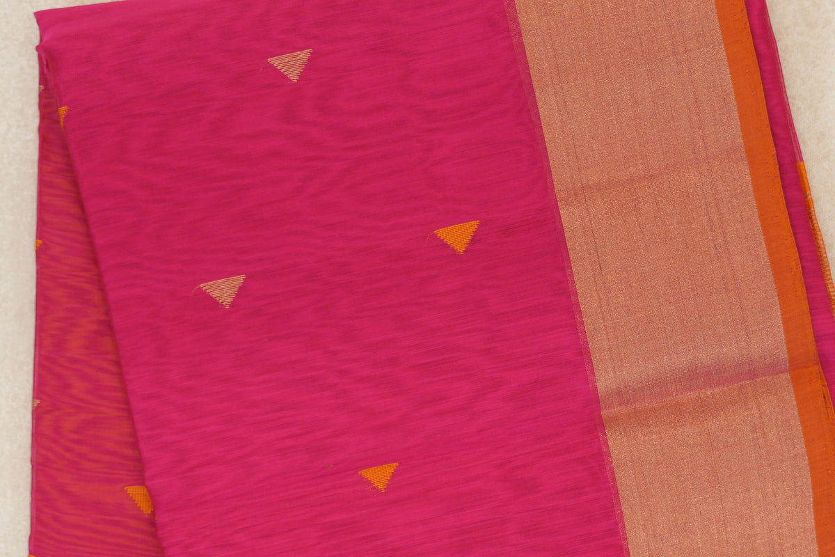 Folded close-up of a rani pink Maheshwari silk cotton saree with small orange triangle motifs and a broad, textured orange border.
