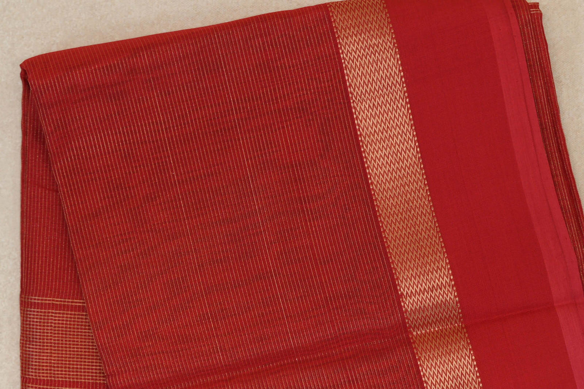 Folded red Maheshwari silk-cotton saree with fine gold-toned stripes and a wide zigzag-patterned border beside a plain red panel.