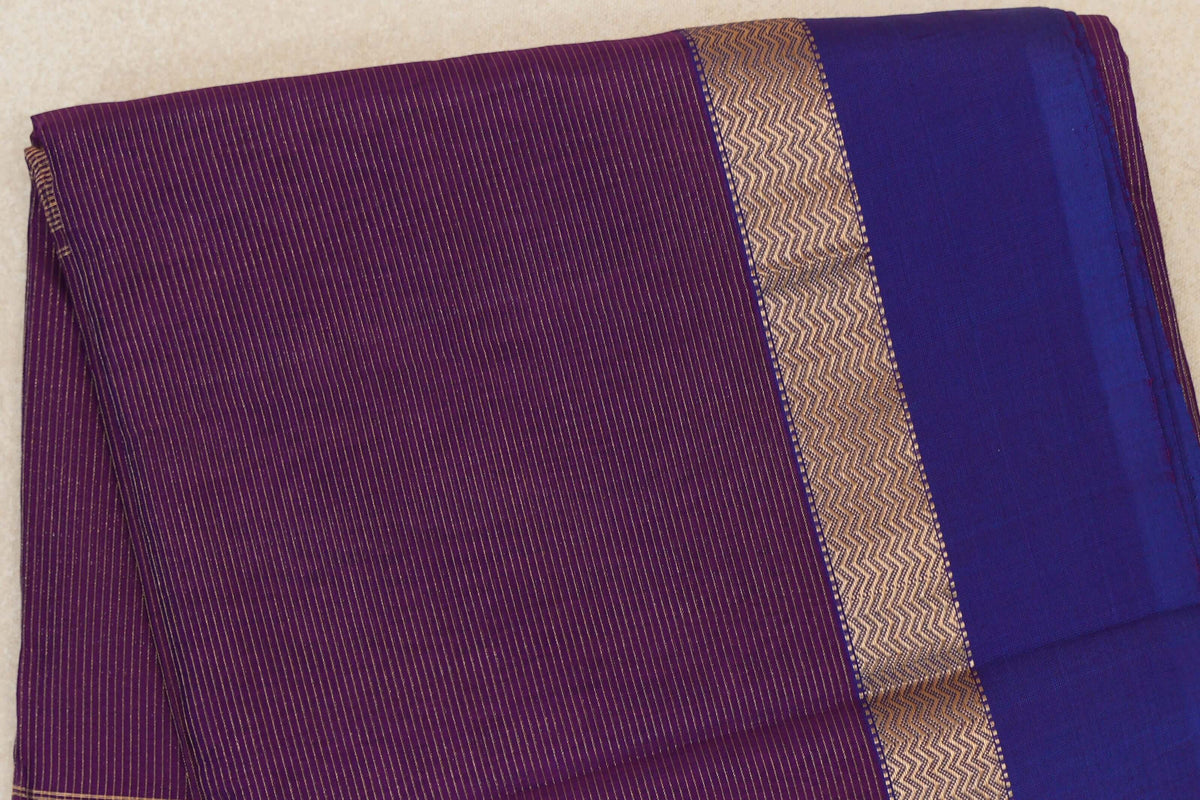 Folded Maheshwari silk cotton saree with fine gold stripes on deep purple, a gold zigzag band and a wide violet purple border.