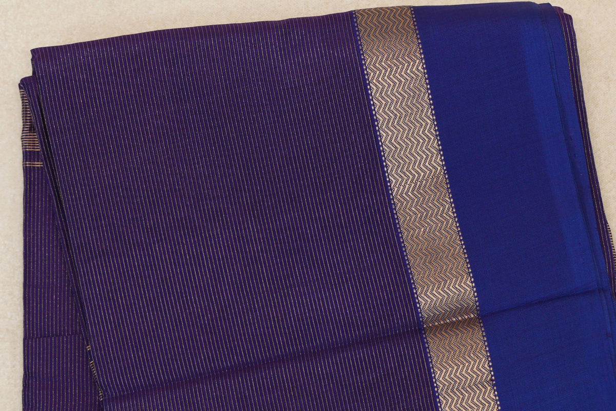 Folded Maheshwari silk cotton saree with fine gold-toned stripes on deep purple and a zigzag-patterned band beside a plain violet border.