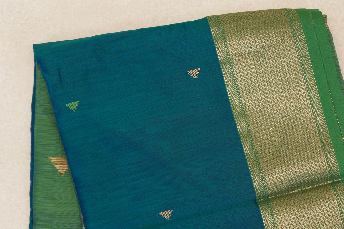 Folded Maheshwari silk-cotton saree with a peacock green body, small triangular motifs and a leaf green border with gold chevron detailing.