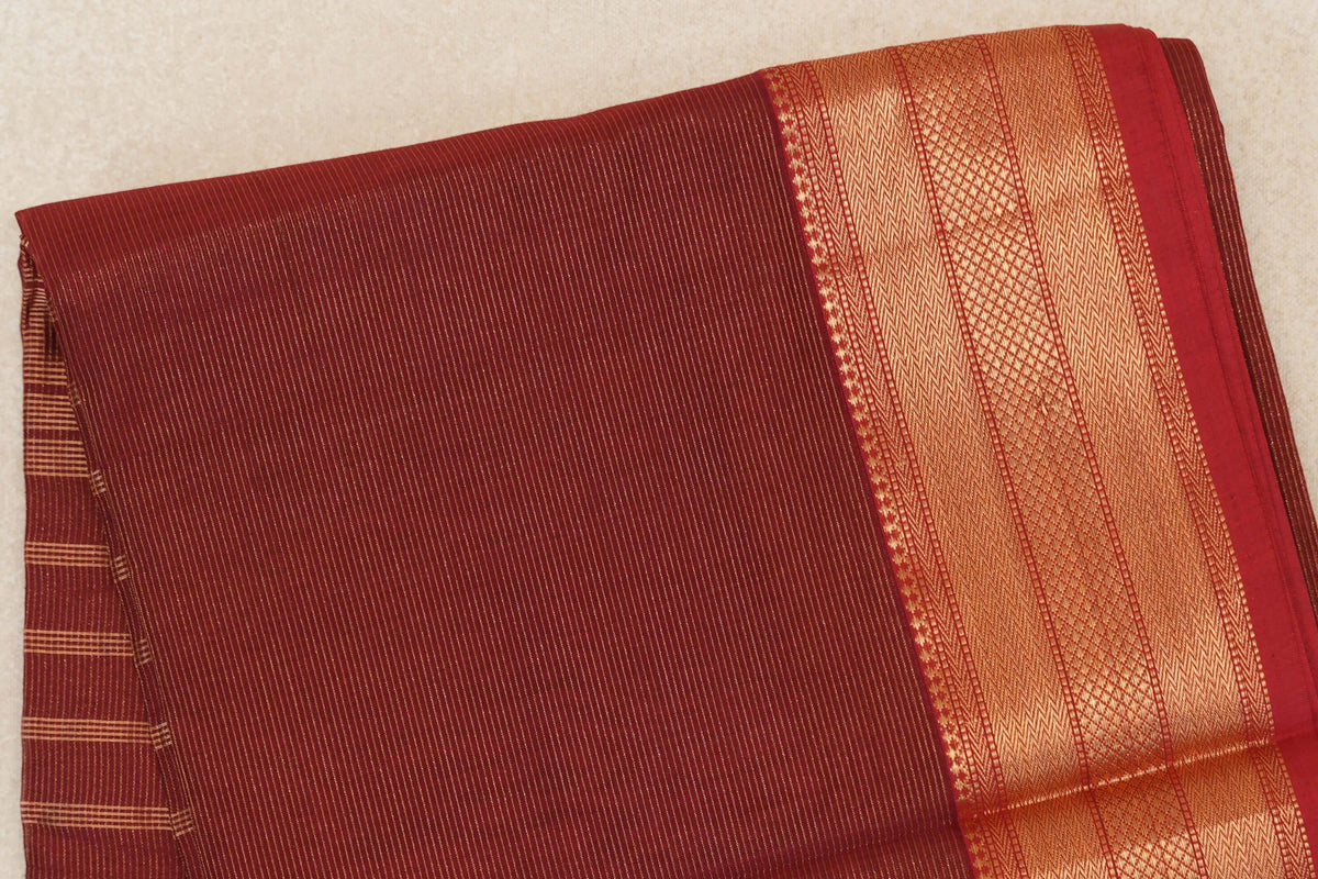 Folded brick red Maheshwari silk cotton saree with fine gold stripes and a wide geometric gold border.
