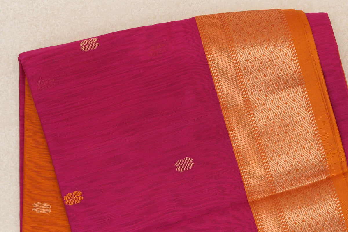 Folded rani pink Maheshwari silk cotton saree with small gold-toned accents and a deep orange border with a shimmering geometric pattern.