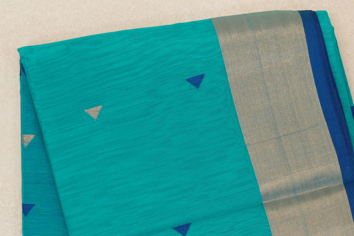 Folded bright turquoise green Maheshwari silk-cotton saree with small blue and silver-toned triangles, a wide shimmering border and Classic Blue selvedge.