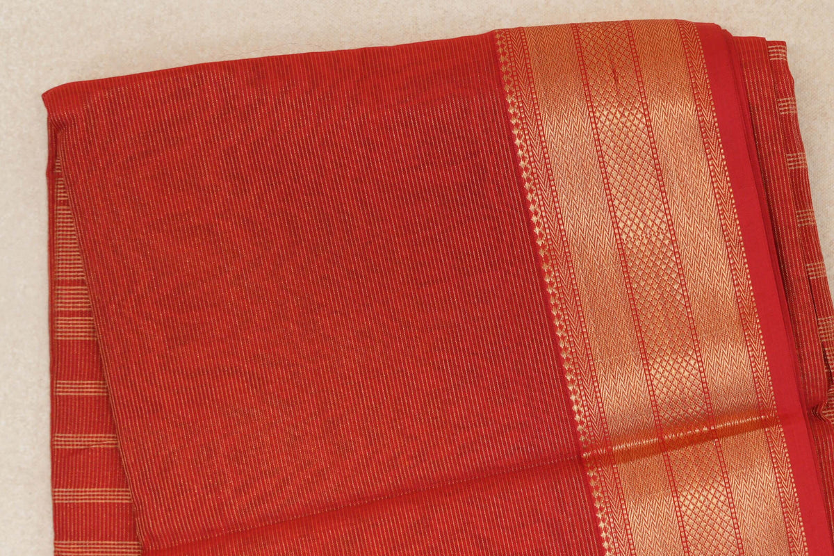 Folded tomato red Maheshwari silk cotton saree with fine gold-toned stripes and a wide border of woven geometric patterns.