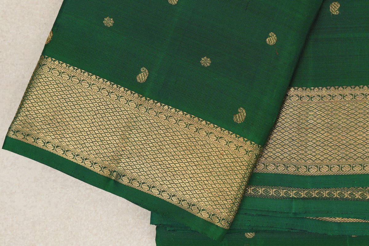 Close-up of folded bottle green Kanjivaram silk saree with scattered gold motifs and a wide, intricately patterned gold zari border.