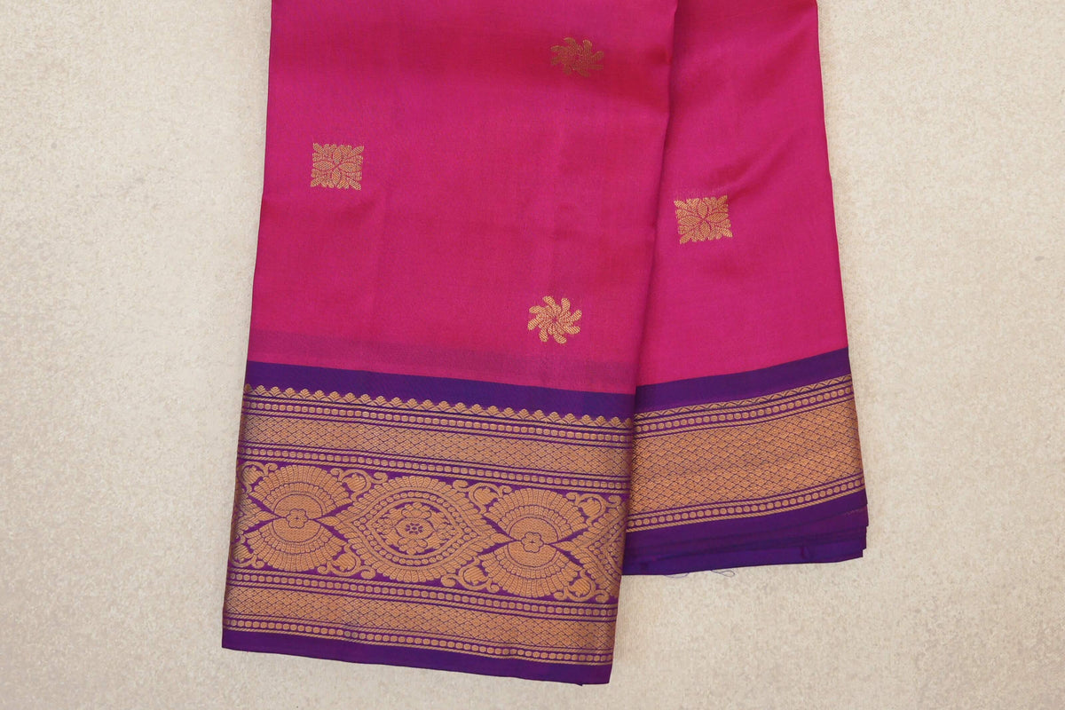 Folded Kanchipuram silk saree showing a rani pink body with scattered gold motifs and a magenta purple border with intricate gold patterns.
