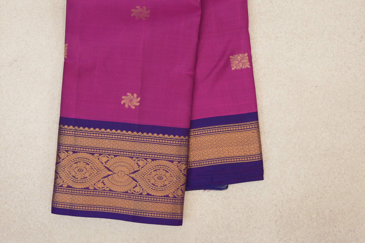 Folded deep magenta Kanchipuram silk saree with scattered gold floral motifs and violet purple borders with gold geometric and floral patterns.