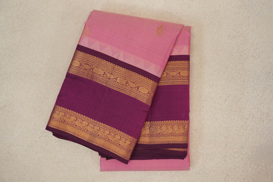 Folded light rose pink Kanchipuram silk saree with small gold motifs and deep magenta borders featuring gold floral bands and pale triangular edging.