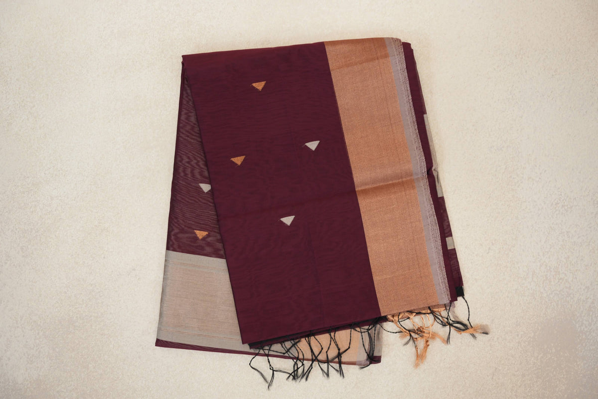 Folded deep wine maroon Maheshwari silk cotton saree with small triangle motifs, a broad warm-toned border, silver grey edge and tassels.