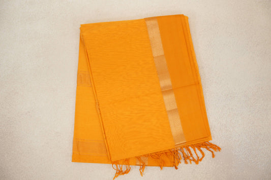 Folded mango yellow Maheshwari silk cotton saree with a subtle striped body, pale chevron border and tassels at one end.