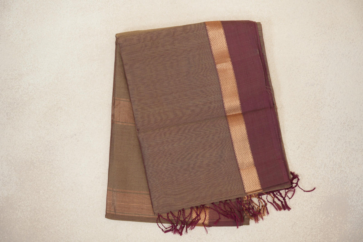 Folded Maheshwari silk cotton saree with a fine beige check, a magenta border edged in gold zigzags, and tassels along one end.