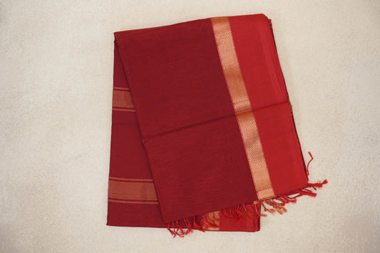 Folded deep red Maheshwari silk cotton saree with fine stripes, a gold zigzag border and red tassels at the edge.