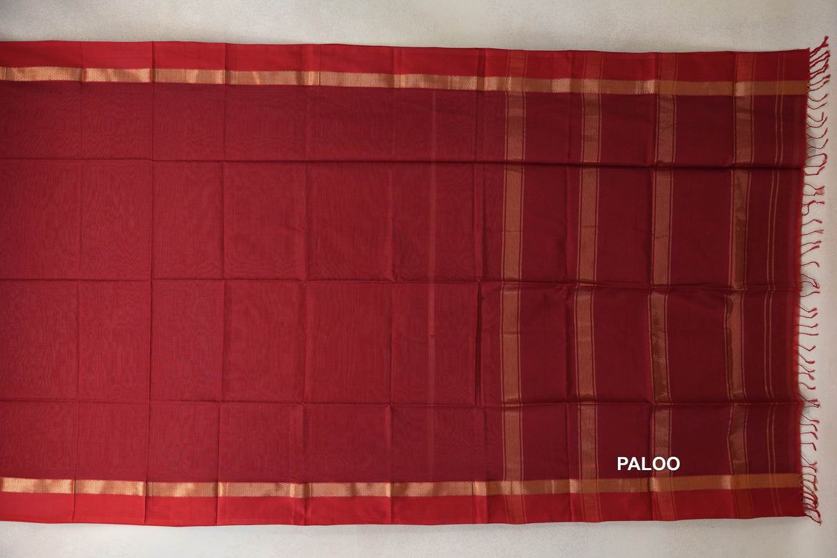Deep red Maheshwari silk cotton saree spread flat, with narrow gold-toned borders and a striped pallu ending in red tassels.