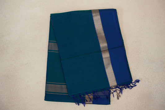 Folded Peacock Blue Maheshwari silk cotton saree showing a plain body, deep Peacock Blue border, metallic zigzag band and tassels.