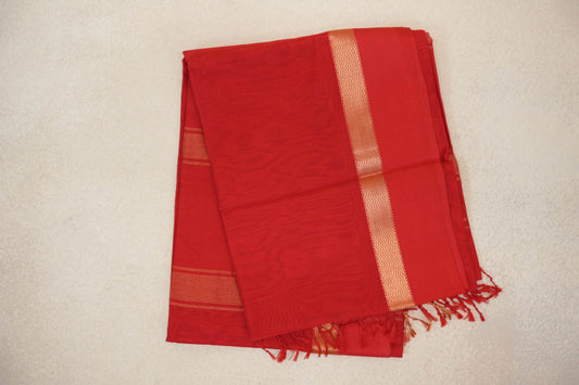 Folded vermilion red Maheshwari silk cotton saree with a gold-toned chevron border, fine stripes on an inner fold, and red tassels.