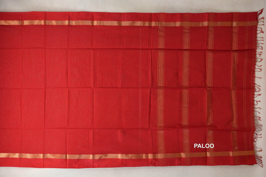 Vermilion red Maheshwari silk cotton saree laid flat, with a plain body, gold-toned border stripes and a striped pallu with tassels at the right.