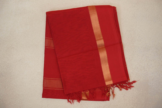 Folded vermilion red Maheshwari silk cotton saree with a fine grid pattern, gold zigzag border, striped detail and tassels.