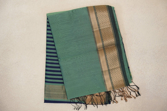 Folded sea green silk cotton saree with a dark sea green and gold zari border, navy-striped pallu peeking out beneath and tassels at the edge.