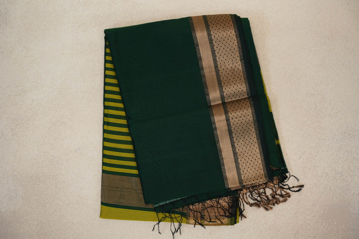 Folded Maheshwari silk cotton saree with a bottle green body, deep green and gold-toned patterned border, olive yellow stripes and tassels.
