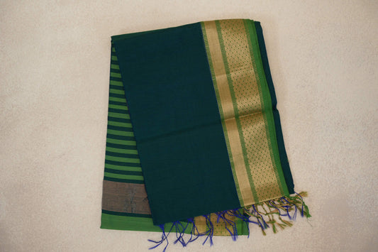 Folded peacock blue Maheshwari silk cotton saree with a leaf green, gold-patterned border, striped pallu peeking out and blue-green tassels.