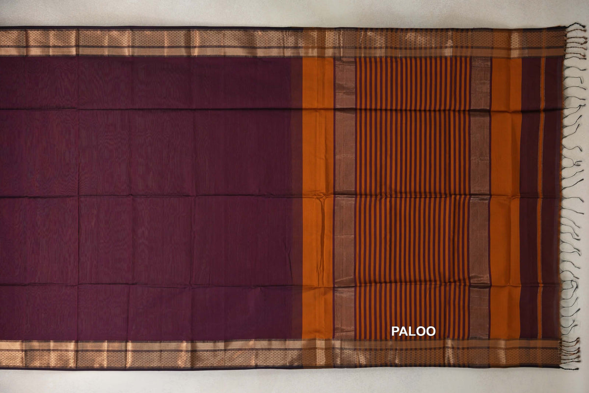 Maheshwari silk cotton saree laid flat, showing a deep plum body, gold-toned patterned borders and a deep orange striped pallu with tassels.