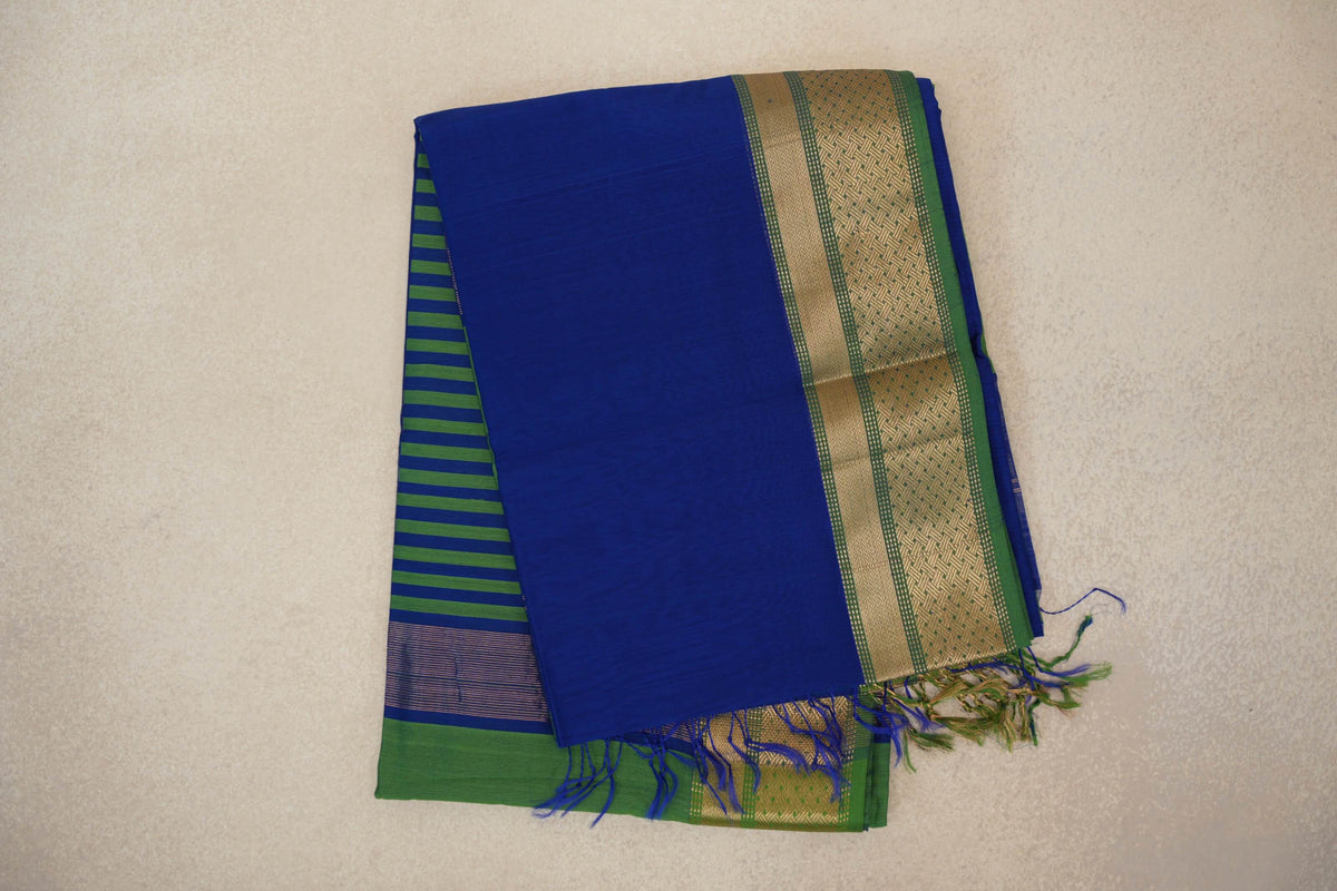 Folded bright royal blue Maheshwari silk cotton saree with a leaf green and gold-toned patterned border, striped pallu peeking out and tassels.