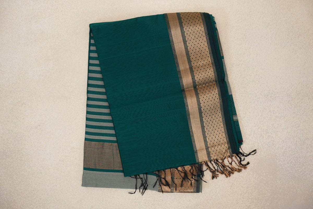 Folded peacock green Maheshwari silk cotton saree showing a geometric border, a silver grey striped pallu and tassels.