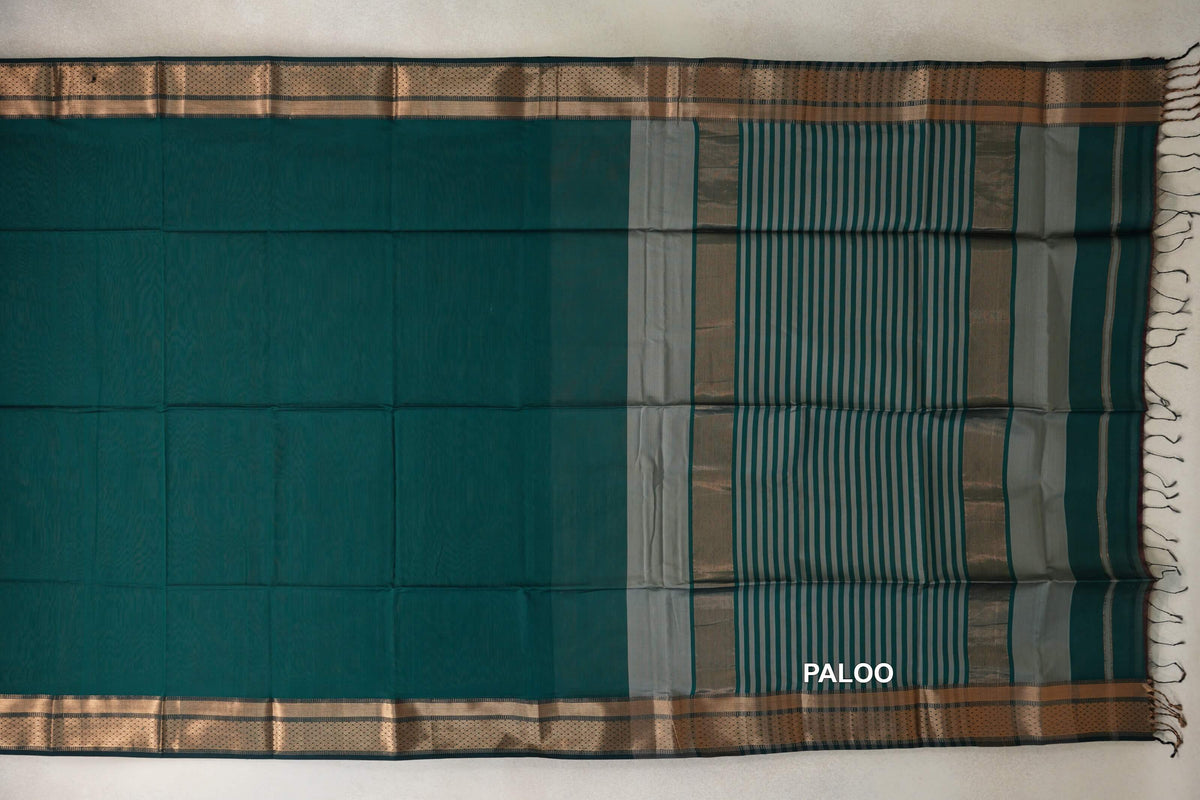 Peacock green Maheshwari silk cotton saree laid flat, with patterned borders and a dark peacock green pallu striped in silver grey, ending in tassels.